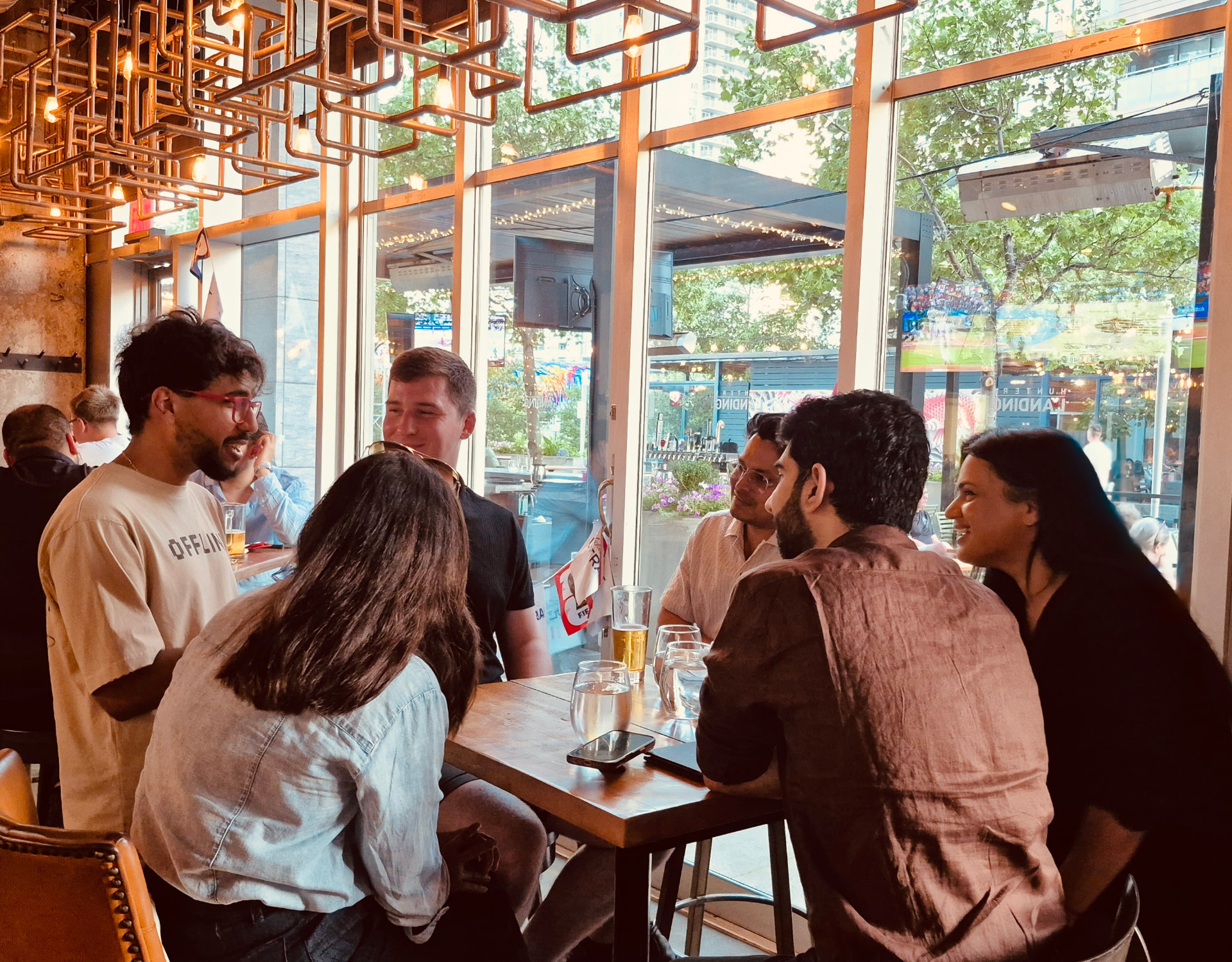Six people laughing together at a high-top table by the windows